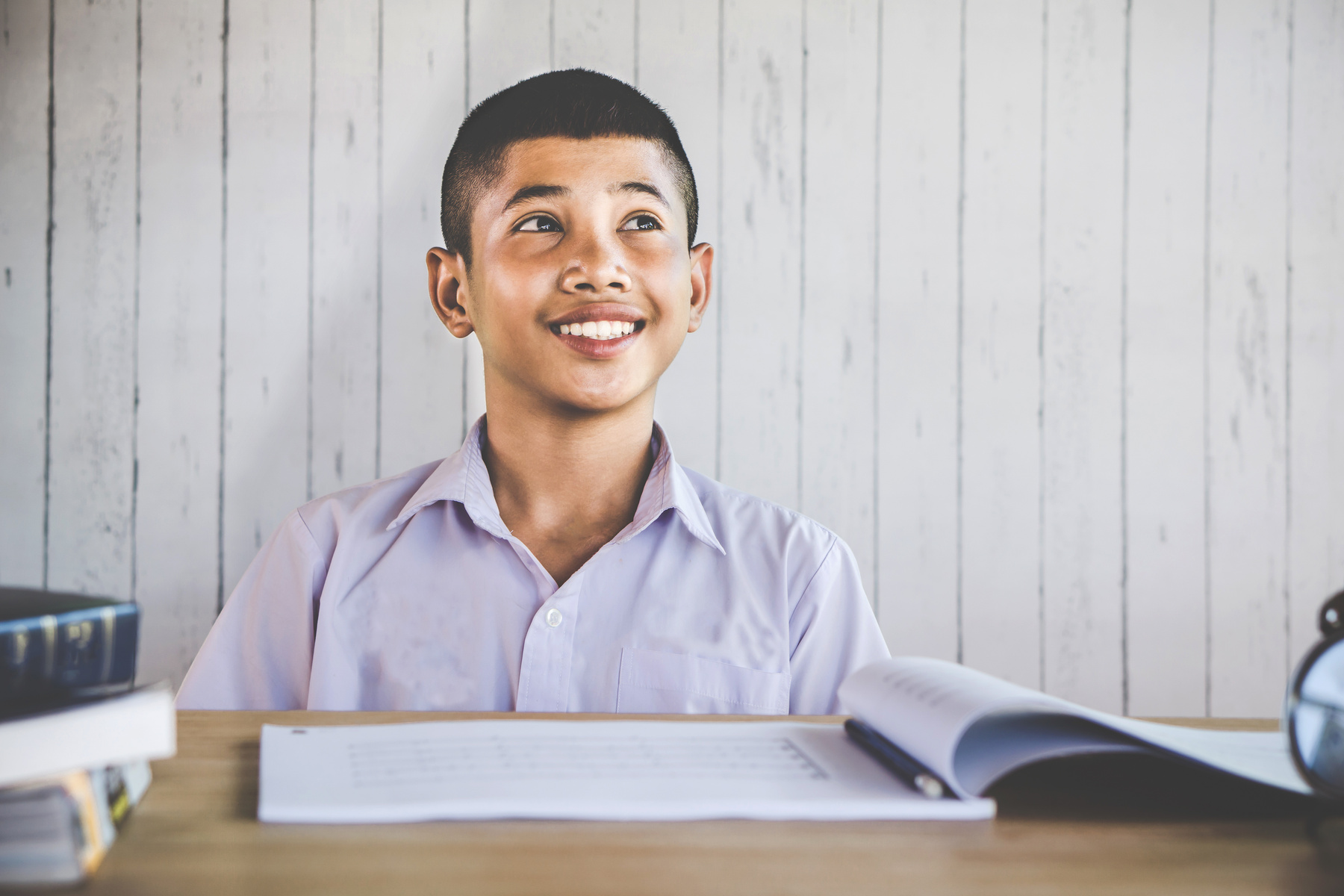 Thai boy student sitting at school desk looking up smiling